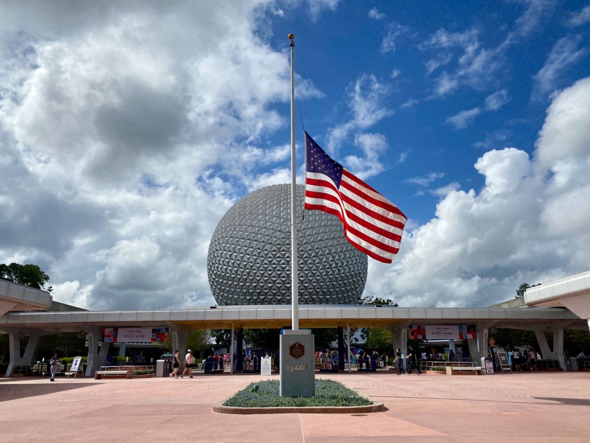 american flag half mast in front of spaceship earth