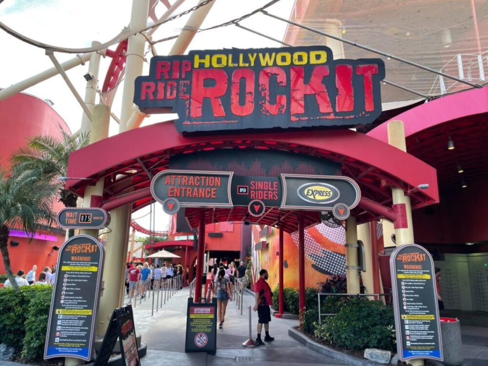 Entrance to Universal Orlando's Hollywood Rip Ride Rockit roller coaster features signs for attraction entrance, single riders, and express pass. People are waiting in line; wait time is 75 minutes.