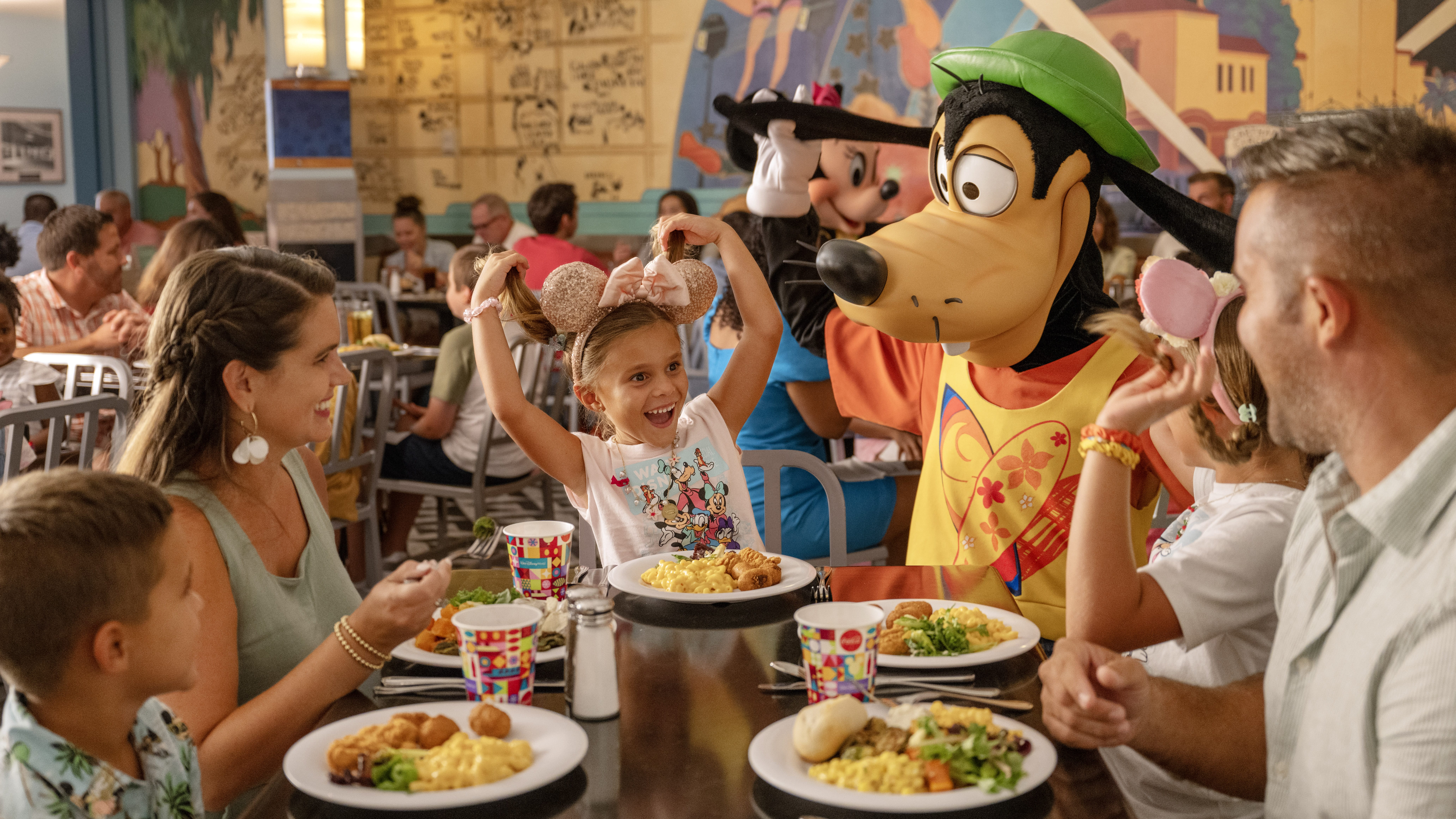 Amid the bustling restaurant, a child wearing mouse ears excitedly interacts with a costumed character. With Disney Deal's 2025 Free Dining Plan, this magical family moment becomes even more enchanting.